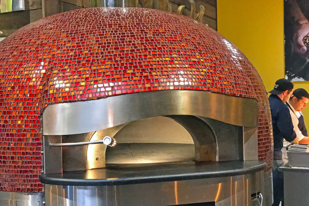 The oversize red-tiled gas- and wood-fired stone oven is a centerpiece of Noosh Nosh’s open kitchen.