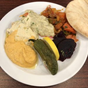 Spicy hummus, regular hummus and baba ganoush (on the left) flank portions of tomato-jalapeño stew, a pita, roasted eggplant, and a roasted jalapeño with lemon.