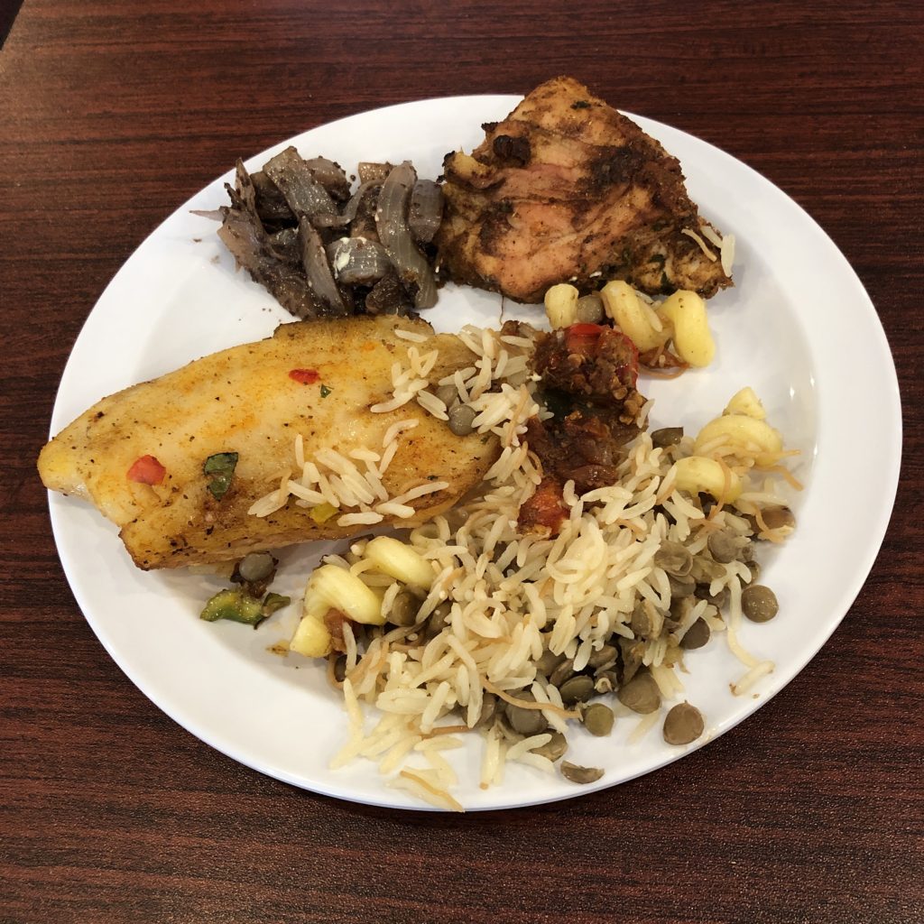Red snapper and sumac-rubbed chicken with sauteed onions flank a porton of kushari, a spicy rice, pasta, and lentil dish.