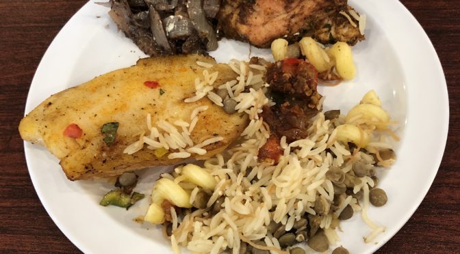 Red snapper and sumac-rubbed chicken with sauteed onions flank a porton of kushari, a spicy rice, pasta, and lentil dish.