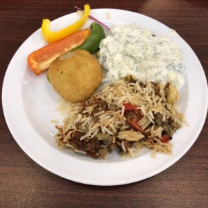 A potato-coated, lamb-filled kubba is accompanied by bright three-color peppers, yogurt and cucumbers, and a portion of rice-and-pasta kushari.