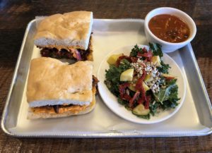 House-made smoked vegan pepperoni on a focaccia sandwich with summer squash salad and chicken chili at The Table.