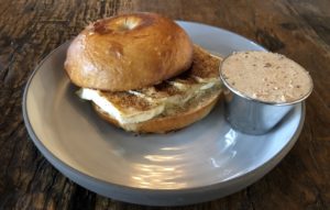 A light, crisply crusted bagel at Butchertown Grocery Bakery bears slices of brie, crushed pecans, and seasonal autumn spice.