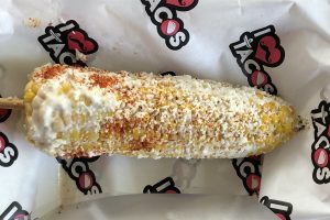 Elotes del barrio at I Love Tacos start with a grilled cob of yellow-and-white corn and paint it with mayo, grated queso fresco, red chile powder and lime juice.