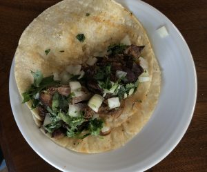 Masita de puerco tacos at I Love Tacos feature tender, citrus-marinated Cuban-style roast pork set up Mexican-style with onion and cilantro on a white-corn tortilla.