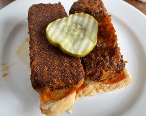 A pair of blocks of Royals Nashville-style hot tofu, crusted and fried, covered with fiery hot sauce,  and served on white bread. 