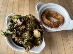 Side dishes at Monnik: earthy, savory brussels sprouts and bacon, and a huge single onion ring.