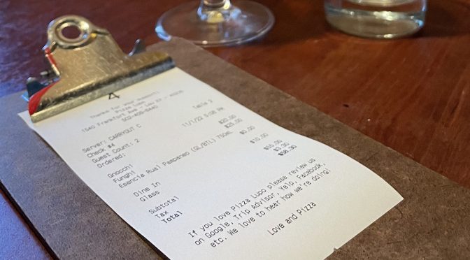 Secured to a clipboard, the tab at Pizza Lupo awaits our payment, with half a glass of a Spanish natural wine to finish.
