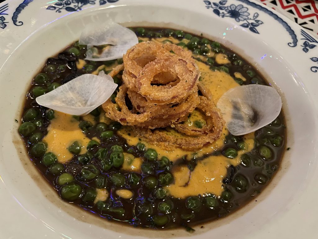 Rouxed peas, a vegetarian dish, celebrate al dente green peas with a dark and spicy black roux and delightful tiny fried onion rings.