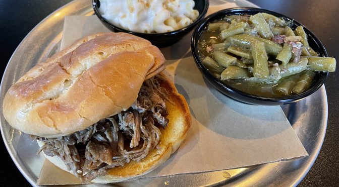 The Smokery's pulled pork is soft and juicy and deeply smoky, falling into thin shreds on a good brioche bun. It's shown with sides of Gouda mac and long-simmered green beans.