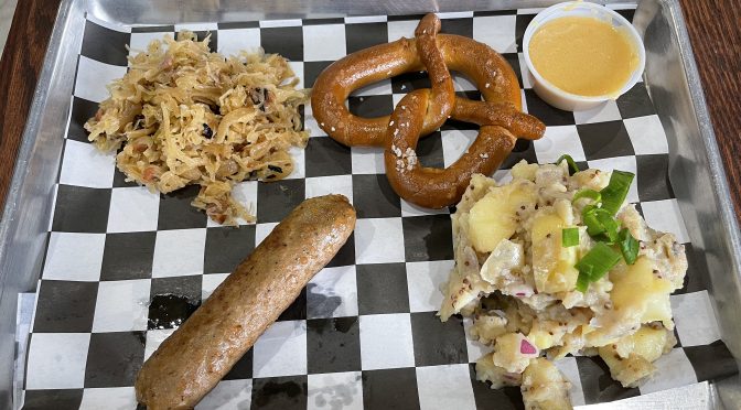 V-Grits in Logan Street Market offers a seasonal Oktoberfest lunch. Clockwise from upper left, apple bacon slaw, a soft pretzel, Wild Hops beer cheese, German potato salad, and a Beyond Meat bratwurst.