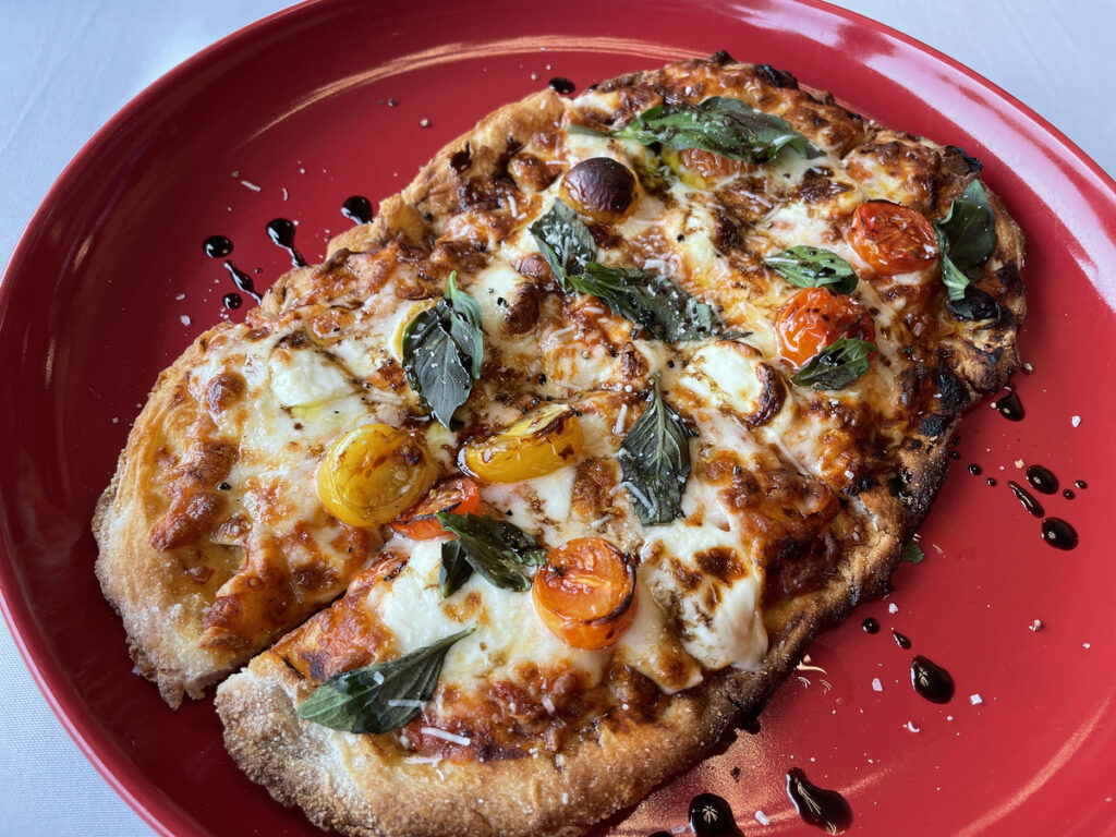 Hand-thrown flatbread forms an oval base red, white, and green tomato sauce, mozzarella, and basil in Osteria's margherita pizza. 